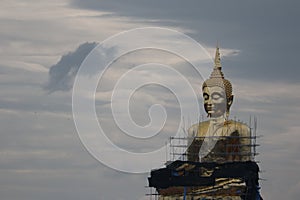 A large golden Buddha image undergoing renovations located outdoors in a Thai temple.