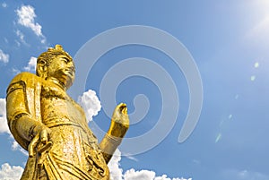 Large golden Buddhist Kannon statue taken from below against a blue sky.