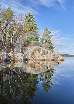 Large granite rock and pine trees reflect in water