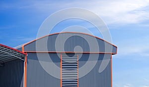 Large gray aluminium industrial warehouse building with curve roof next to pavilion against blue sky background