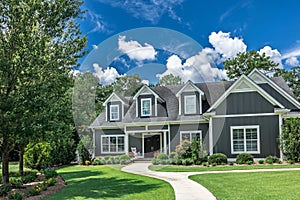 A large gray craftsman new construction house with a landscaped yard and leading pathway sidewalk