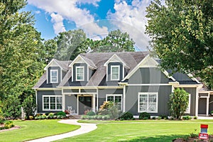 A large gray craftsman new construction house with a landscaped yard and leading pathway sidewalk