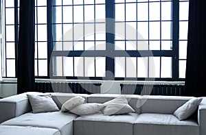 A large gray sofa and large windows with metal bars against a background of concrete walls