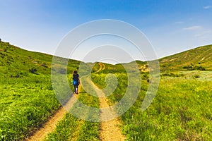 Large green field with a road in the center and a girl on it. Beautiful view of the field with a blue sky