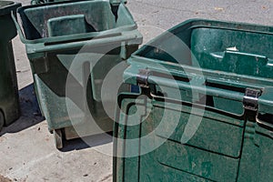 Large green trash cans, empty with lids open, curbside