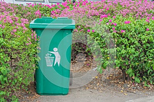 Large green wheelie bin at public park with bush. photo