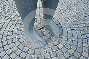 Large grey feet of statue with cobblestone ground