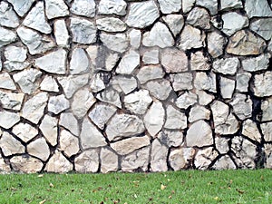 large grey stone wall and backyard green grass lawn