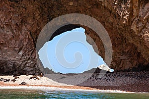 Large through grotto with a beach on which sea lions lie. Through the grotto, birds in the sky Ballestas Islands