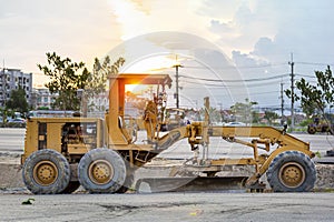 Large ground leveling machine or grader for road or street highway making park at work place with sunset at evening