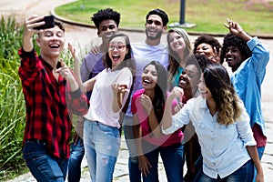 Large group of funny multi ethnic young adults taking crazy selfie with phone
