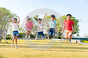 Large group of happy Asian smiling kindergarten kids friends holding hands playing and jumping together during a sunny day in