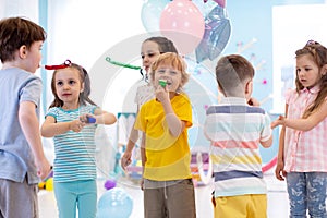 Large group of kids age 3 to 5 inside on a birthday party blowing noisemakers horns and twisted whistles