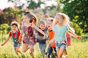 Large group of kids, friends boys and girls running in the park on sunny summer day in casual clothes .