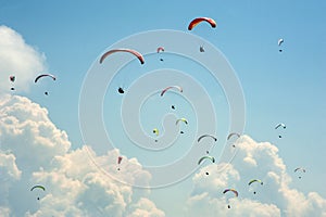 A large group of paragliders flies in the sky against the background of clouds.