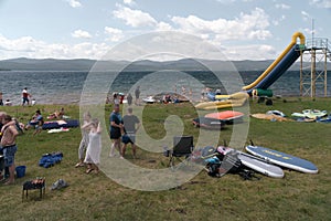 A large group of people are resting on the shore of the Big Lake during their summer vacation