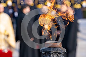 Large group of people walking past a brightly lit torch that is engulfed in flames