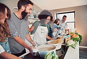 Large group of six friends cooking pasta at table photo