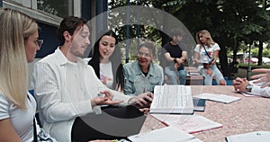 Large group of students sharing knowledge on a sunny day outside of the college campus sitting on a bench