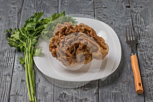 A large gyromitra on a white plate with a fork and herbs.