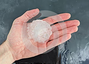 Large hailstone measuring greater than two inches sitting in a personâ€™s hand.
