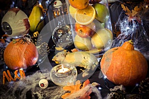 Large halloween decoration table with pumpkins, pine cone, a rat, candles, eyes, a light garland, a vase with fruits and cobwebs