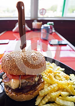 A large hamburger with French fries with a knife on a black plate on a red table in a biker cafe in Greece