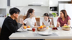 A large, happy Asian family spends time dining at a table in their home. Cute little daughter having fun chatting