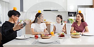 A large, happy Asian family spends time dining at a table in their home. The little daughters chatted and played games for free