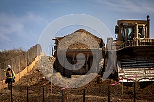 large haul dump truck at a construction site with a worker nearby as well as a bulldozer