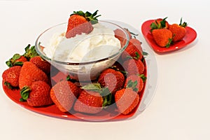 A large heart shaped plate filled with strawberries and a smaller one behind