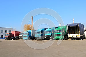 Large heavy cargo trucks with cabs and trailers stand in a row ready for delivery of cargo at the industrial refinery