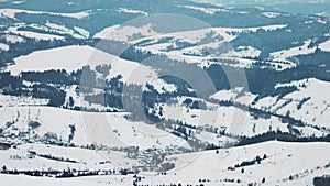 Large hills covered with a carpet of snow and fir forests against the backdrop of a cloudy sky and sunset