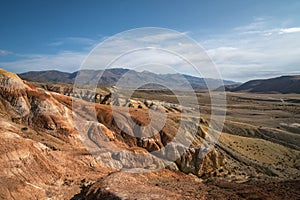 Large hills of red and yellow clay, traces of erosion, rocky surface and sparse vegetation