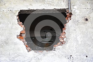 Large hole in an old brick wall. There\'s a lantern hanging behind wall