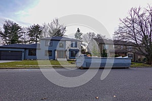 Large home on a residential street with a long blue dumpster on the road in front.