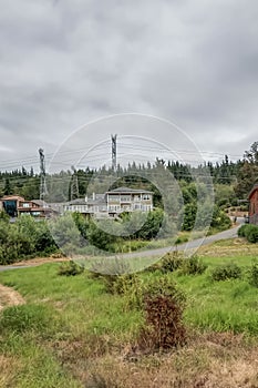Large home surrounded by trees and forest and grass with overcast sky and large power lines