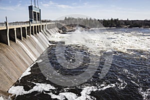 Large hydro dam with water flowing over turbines in summer time.