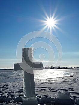 Large ice cross near the hole on the background of blue sky and endless frozen river
