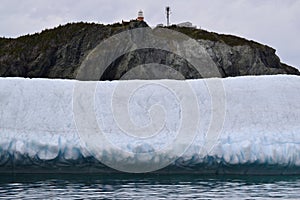 Large iceberg at the base of cliff in Twillingate Harbour with Long Point Lighthouse at the top