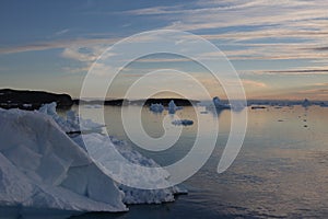 A large iceberg in the foreground with many icebergs in the background at sunset in northwest Greenland