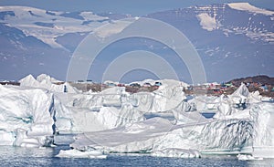 Large icebergs in front of the small community of Saqqaq with towering mountains behind in Disko Bay, Greenland