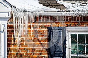 Large icicles hanging from snow covered roof of brick house indicating poor roof insulation