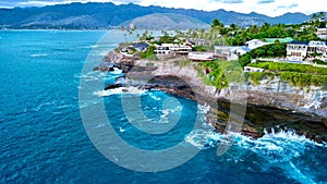 Large, imposing cliff overlooking the ocean, dotted with homes perched atop its rocky cliffs: Hawai