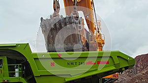 A large industrial excavator in a coal quarry loads rock into a dump truck