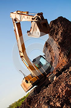 A large iron excavator bucket collects and pours sand rubble and stones in a quarry at the construction site of road facilities