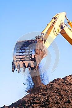 A large iron excavator bucket collects and pours sand rubble and stones in a quarry at the construction site of road facilities