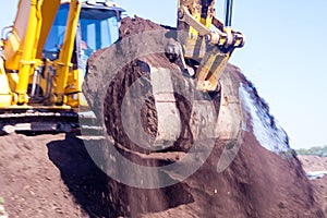 A large iron excavator bucket collects and pours sand rubble and stones in a quarry at the construction site of road facilities