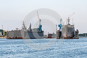 Large iron navy ships in shipyard for repair. Big crane in dockyard. Blue sea harbor