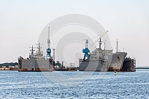 Large iron navy ships in shipyard for repair. Big crane in dockyard. Blue sea harbor